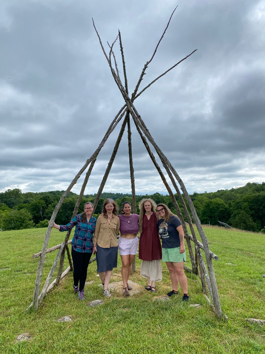 Five herbalists stand under a stick structure.